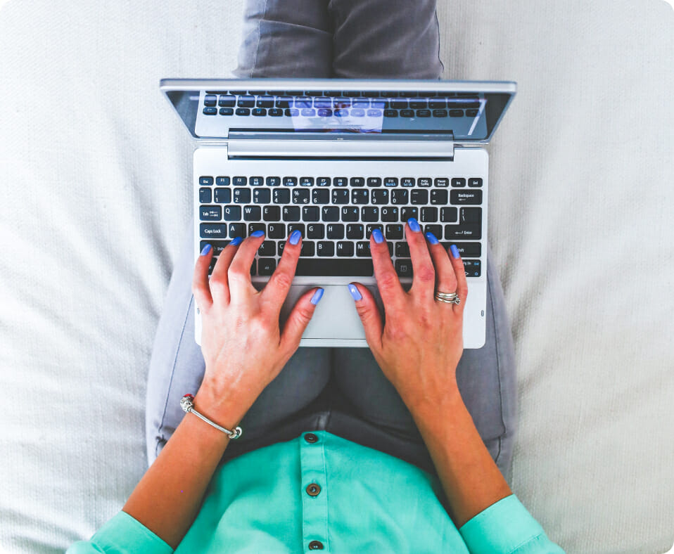 Woman sitting on bed typing on laptop computer.