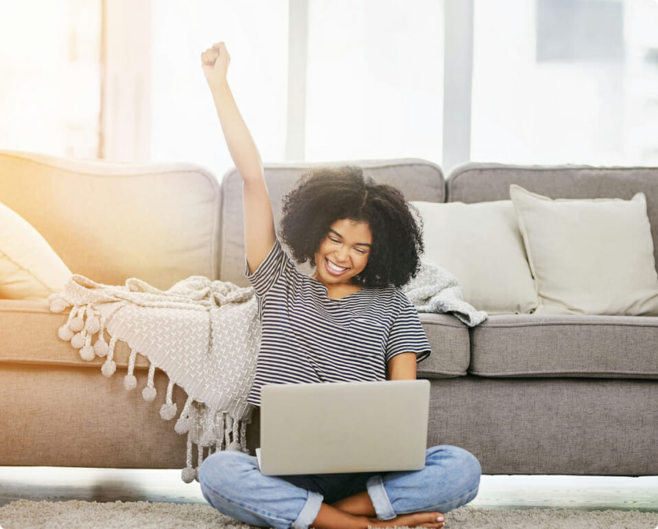 Woman sitting on the floor with a laptop and her fist raised triumphantly after completing Free CPE Courses.