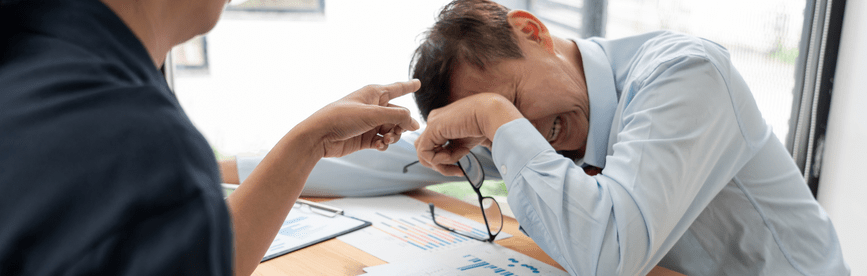 Man at a desk crying while being yelled at, one of the qualities of a bad leader